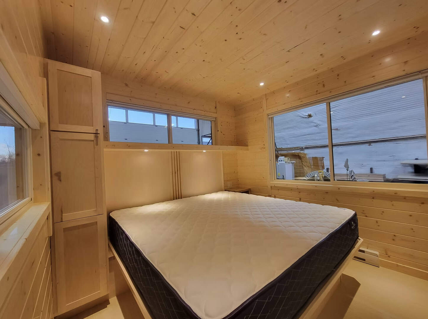 Cozy tiny house bedroom with wooden walls and large windows.