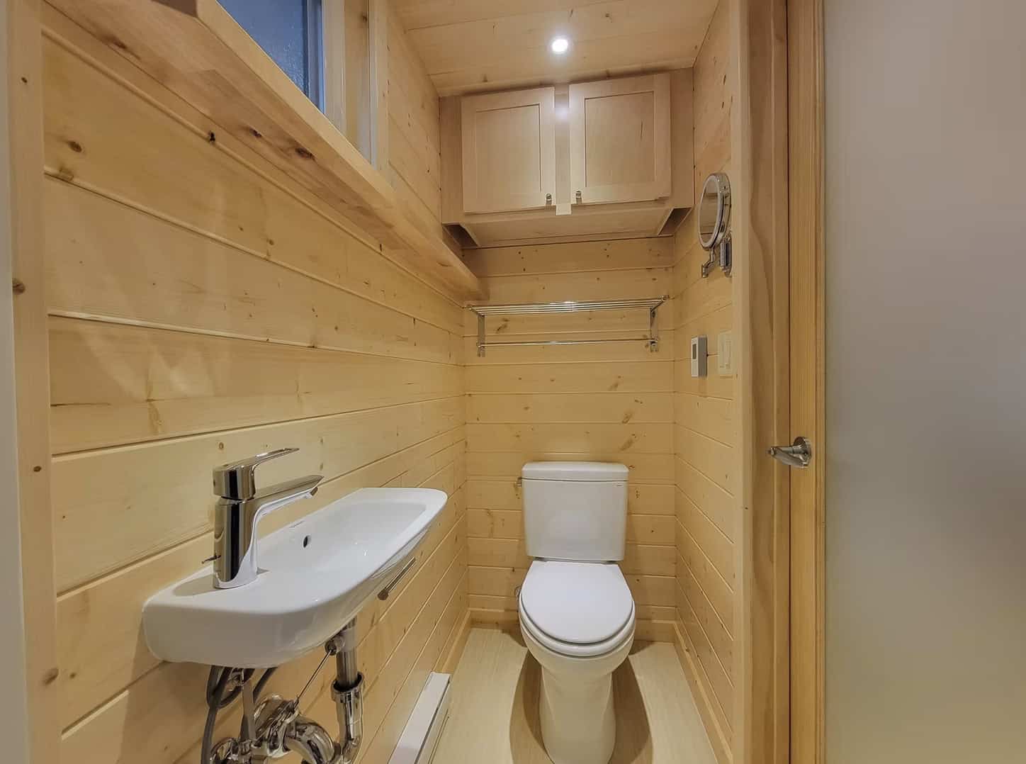 Small wooden tiny house bathroom with toilet and sink.