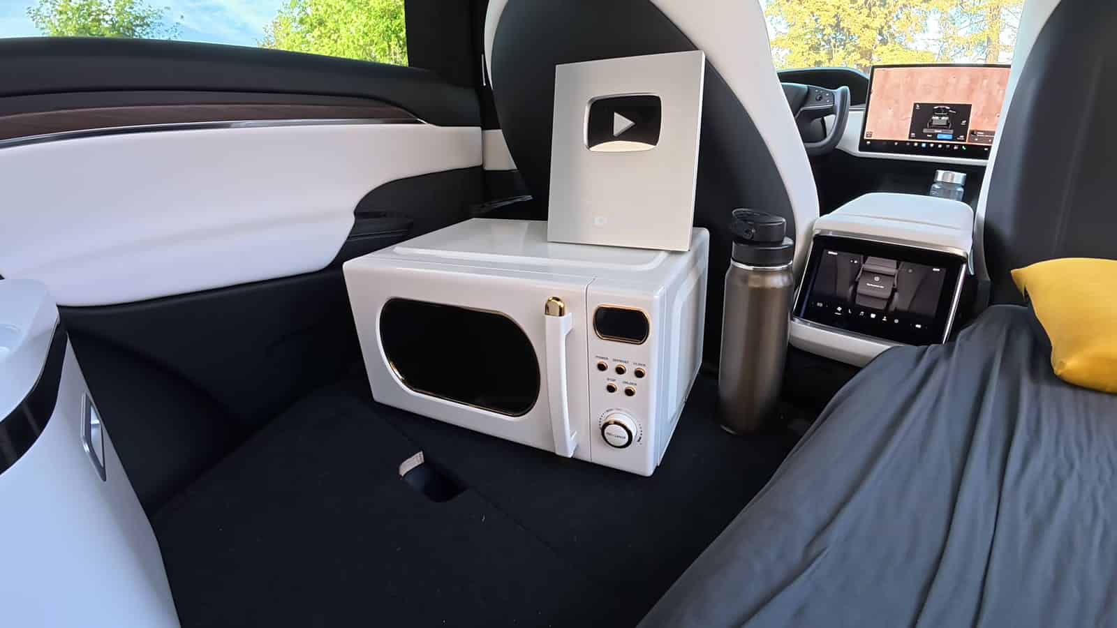 Retro microwave and YouTube silver play button between the front seats of a Tesla Model X camper