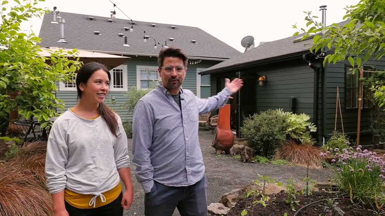 Becca and Anthony in a gravel courtyard with the green ADU at right, main house behind, garden bed, chiminea, and string lights