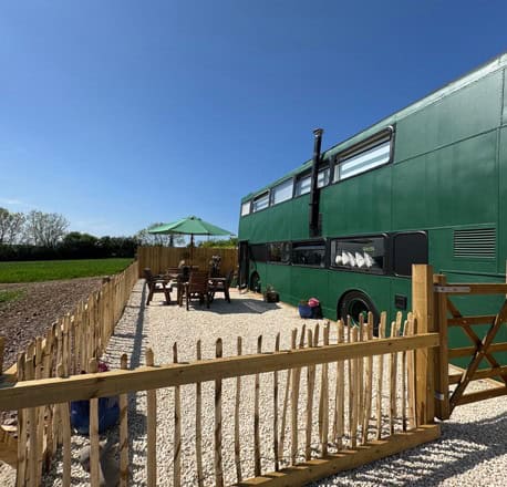 Side of a green double-decker bus with a flue, patio table, and a green umbrella