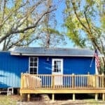 Charming tiny blue house with a wooden deck, nestled among trees in Florida. Perfect small space for.