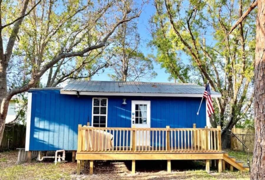 Charming tiny blue house with a wooden deck, nestled among trees in Florida. Perfect small space for.