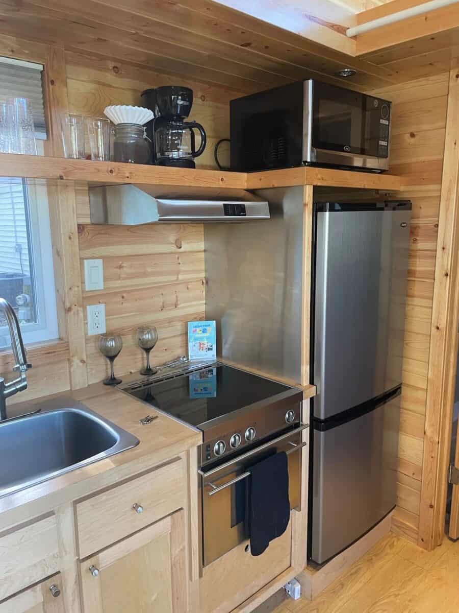 Small kitchen in a tiny home with wooden cabinets, fridge, microwave, and stove.