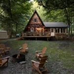 A-Frame cabin nestled among trees with outdoor seating and fire pit.