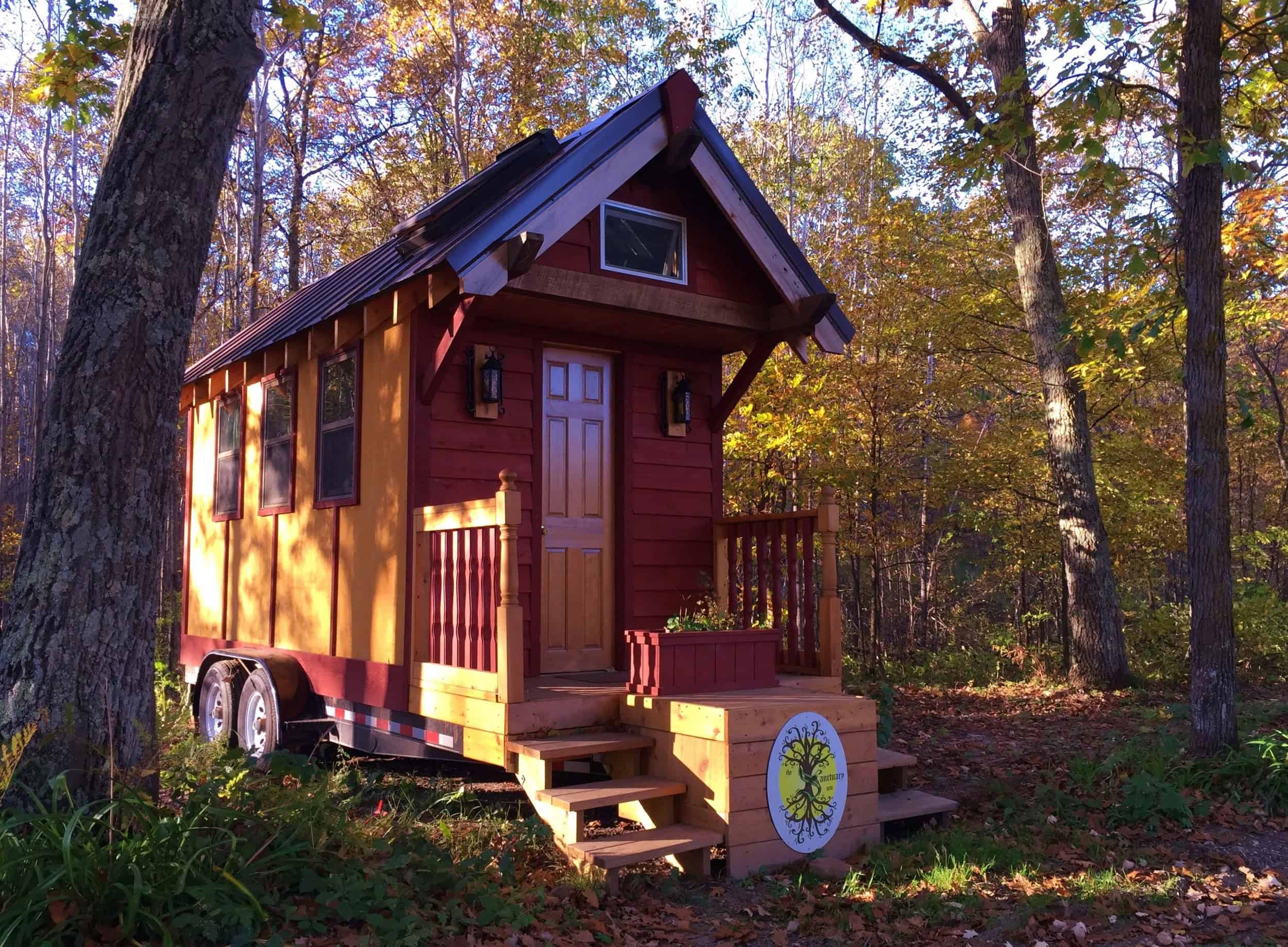 Red and yellow tiny house on wheels beside a Sanctuary MN porch sign at The Sanctuary Minnesota in Ogilvie