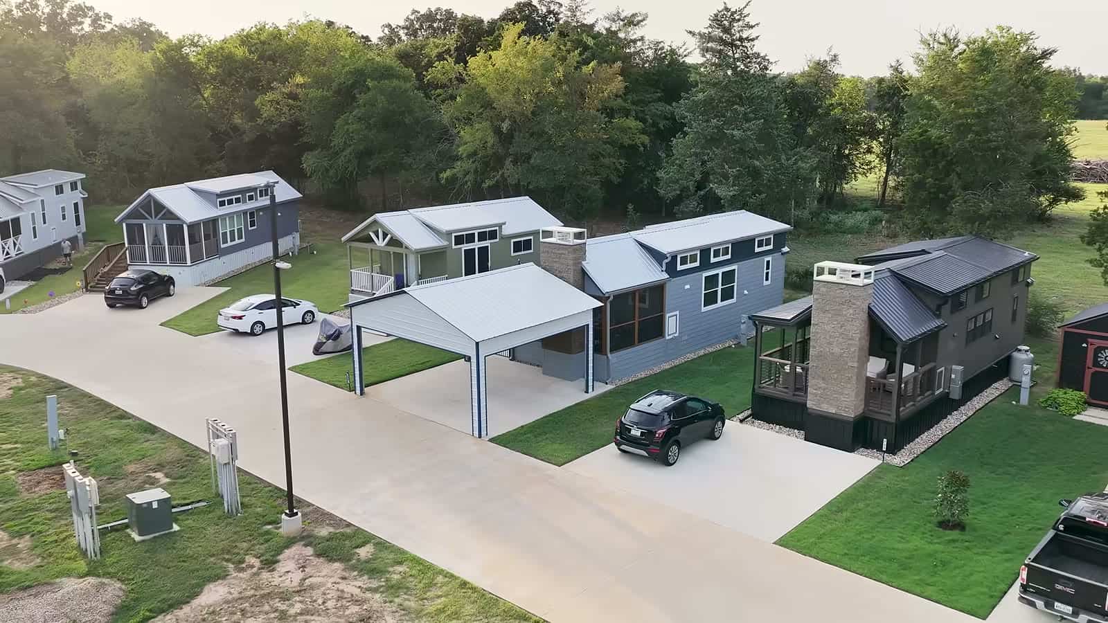Aerial view of park model tiny homes with carports, driveways and lawns along a street at The Oaks on 37