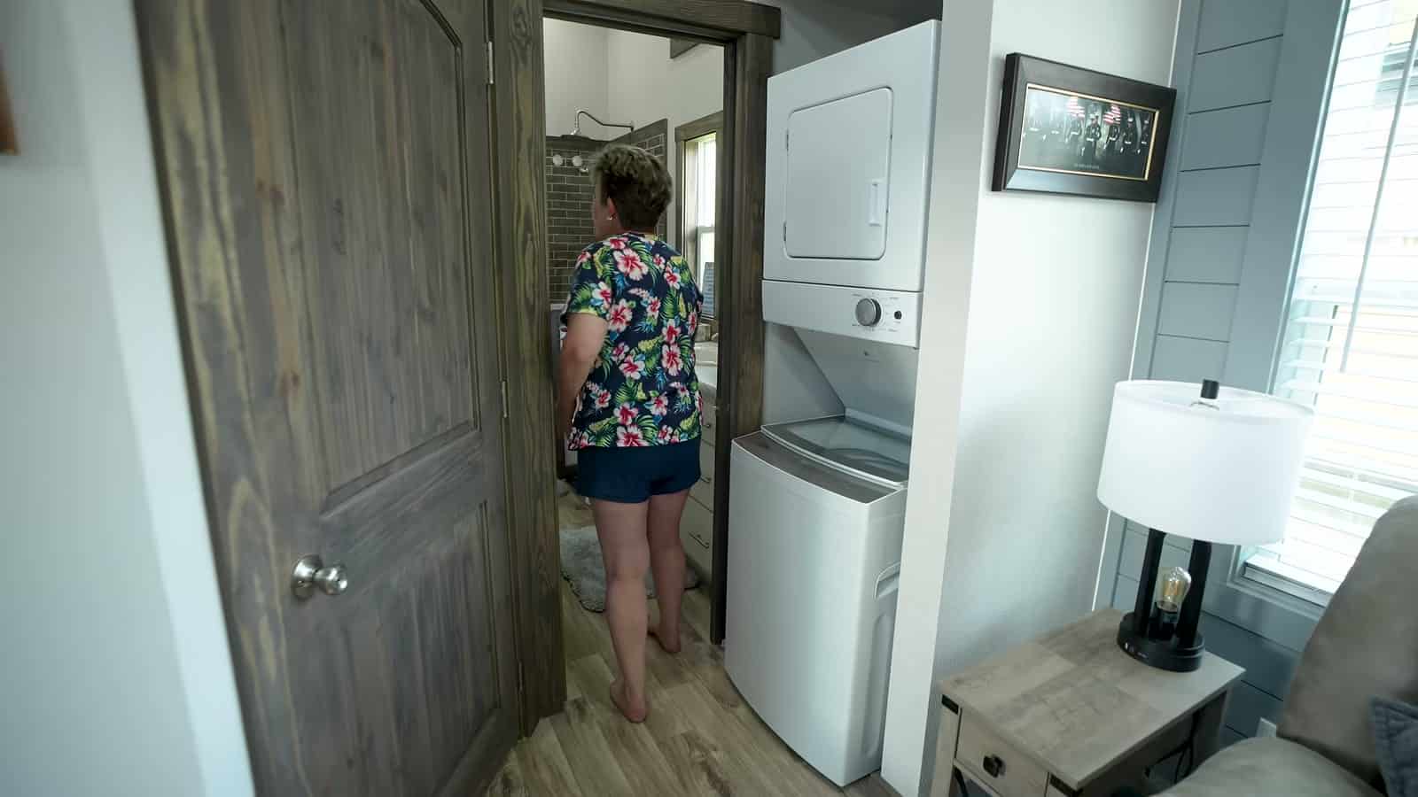 Park model bathroom with white vanity, drawers, toilet, window and brick-look tile shower wall