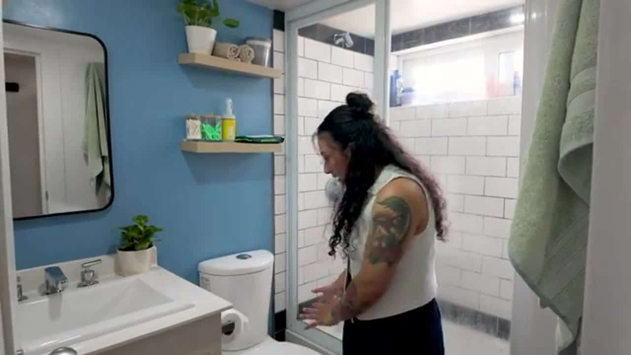 Bathroom with a white vanity, black-framed mirror, toilet, and a glass-door shower with subway tile