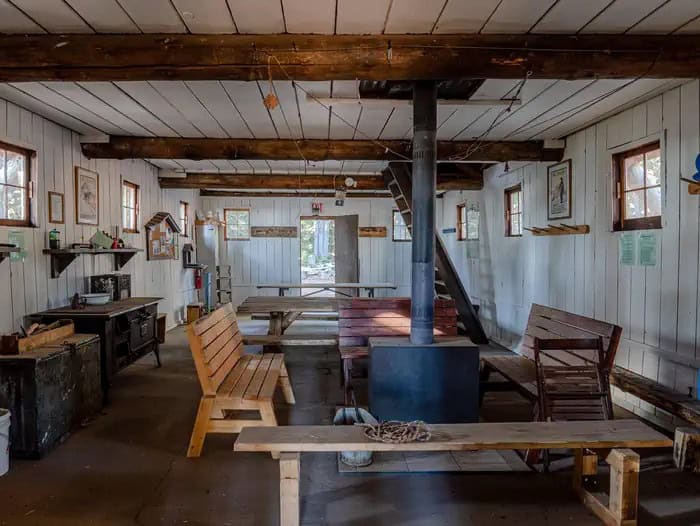 Interior of the Tilly Jane A-Frame: wood stove and flue, benches, a long table, a cookstove along the wall, and a ladder to the sleeping loft