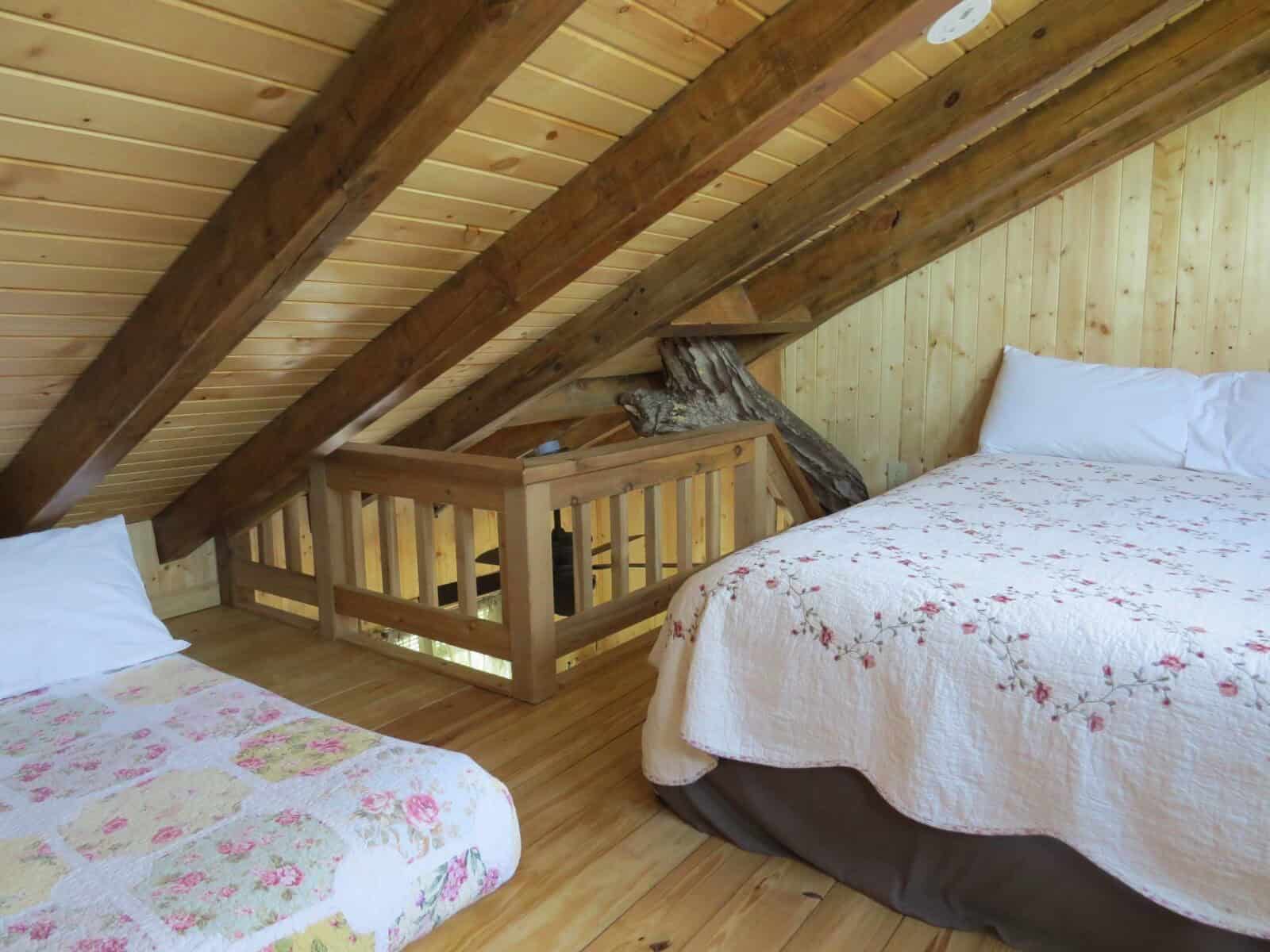 Loft interior with two beds, rafters, and a tree branch at the railing inside the White Oak Treehouse