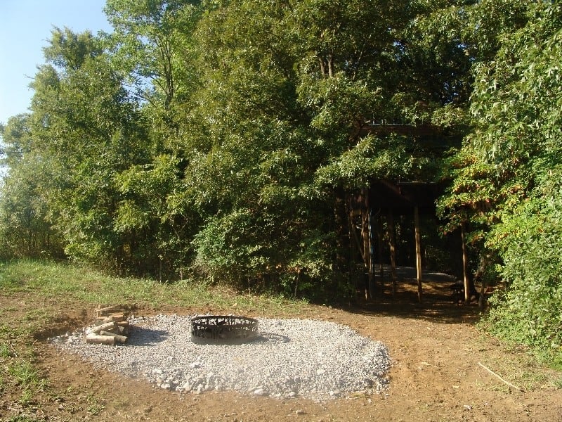 Campfire ring with gravel surround at the edge of the woods near the treehouse