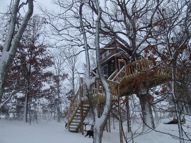White Oak Treehouse in the snow with its staircase and wraparound deck