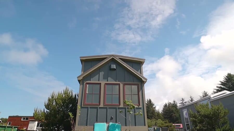 Gable end of the blue board-and-batten Timbercraft tiny home with red-trimmed windows