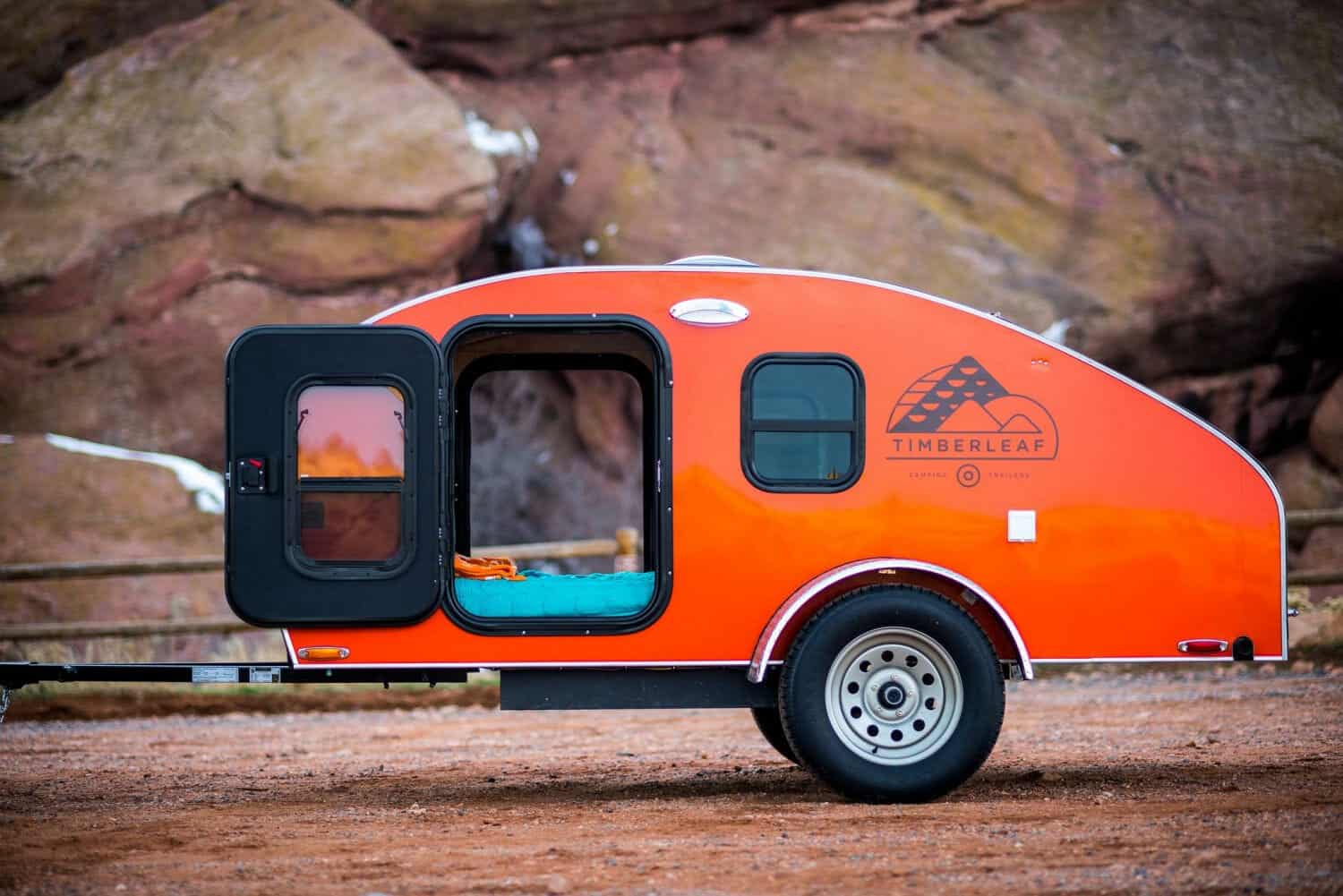Orange Timberleaf Classic teardrop with side door open showing cabin berth against red rock