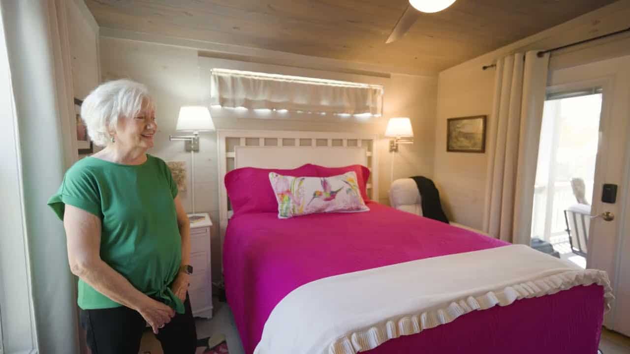 Bedroom with a pink bedspread, white headboard, and a French door to the porch