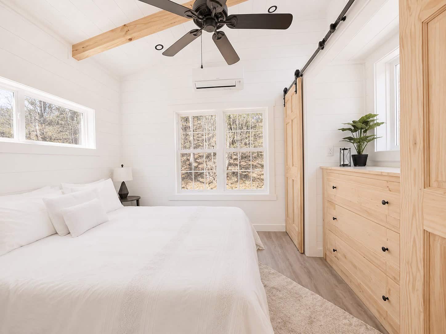 Bedroom with a white bed, ceiling fan, grid window, barn door, and a light wood dresser