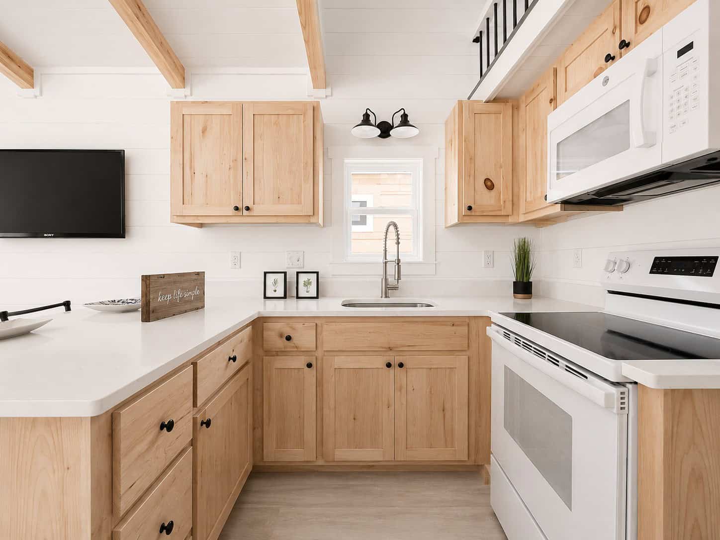 L-shaped kitchen with light wood cabinets, white counters, a sink under a window, and a white range