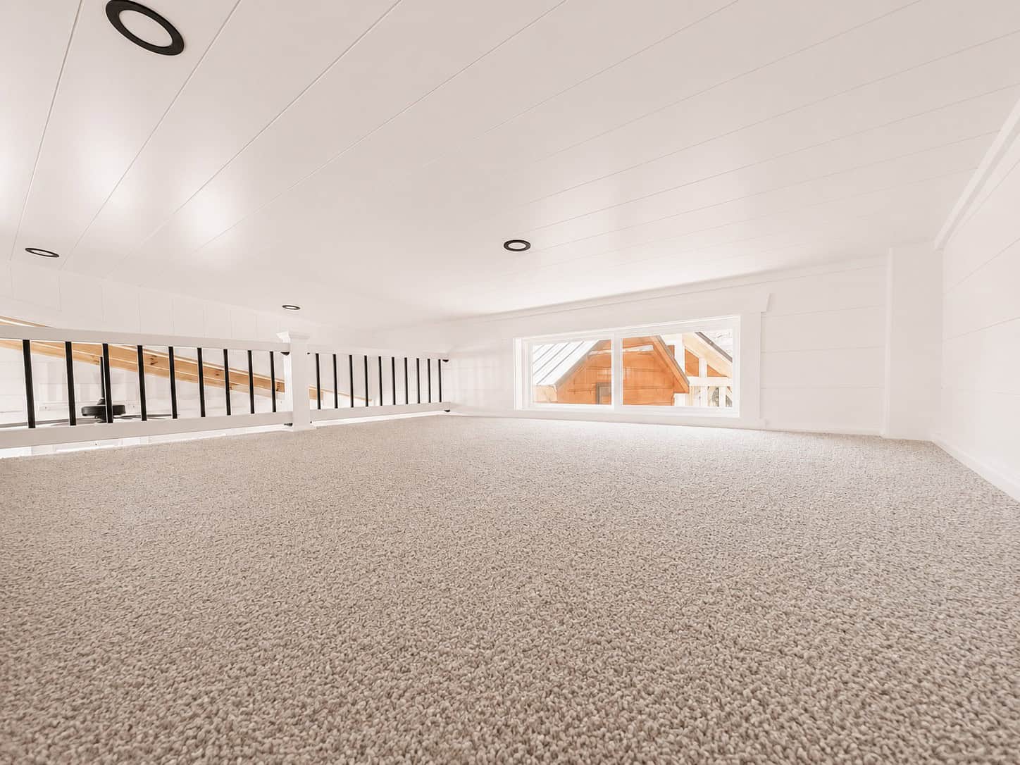 Open carpeted loft with a long rail and a wide window