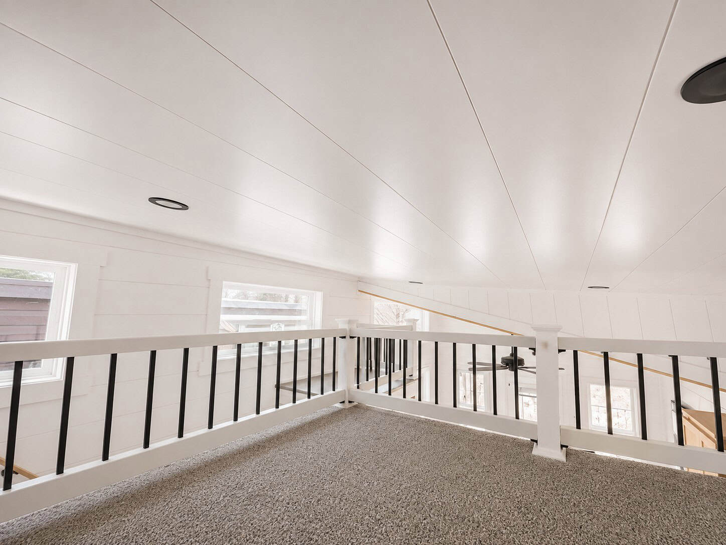 Carpeted loft with a white rail and black spindles looking down to the main floor