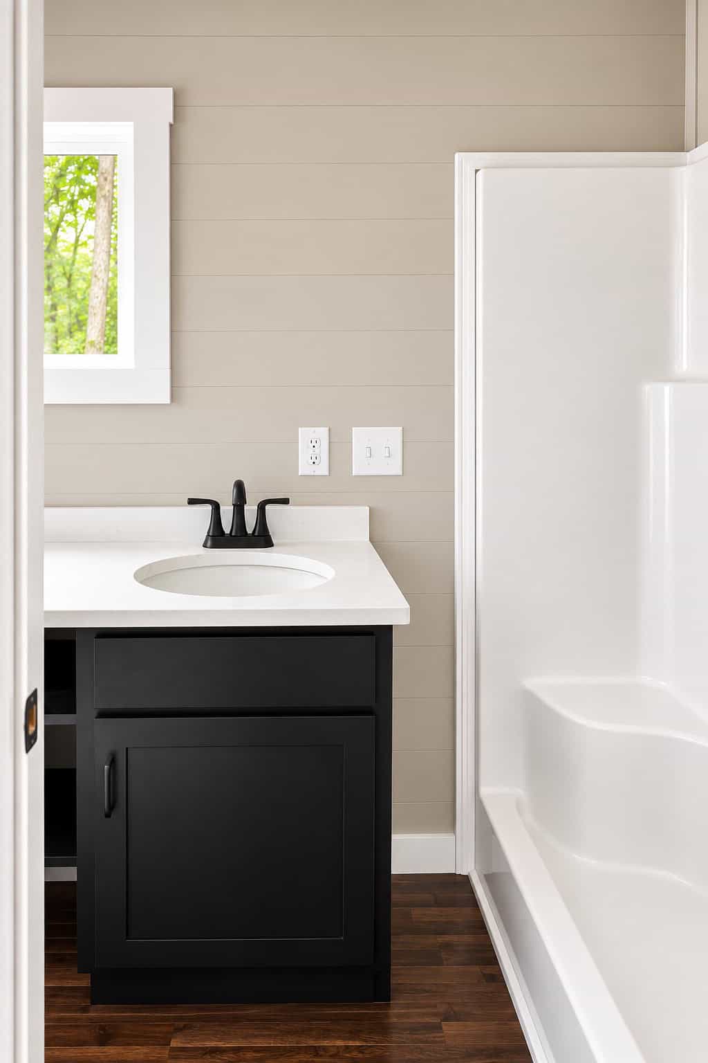 White one-piece tub and shower beside a dark vanity with a white top
