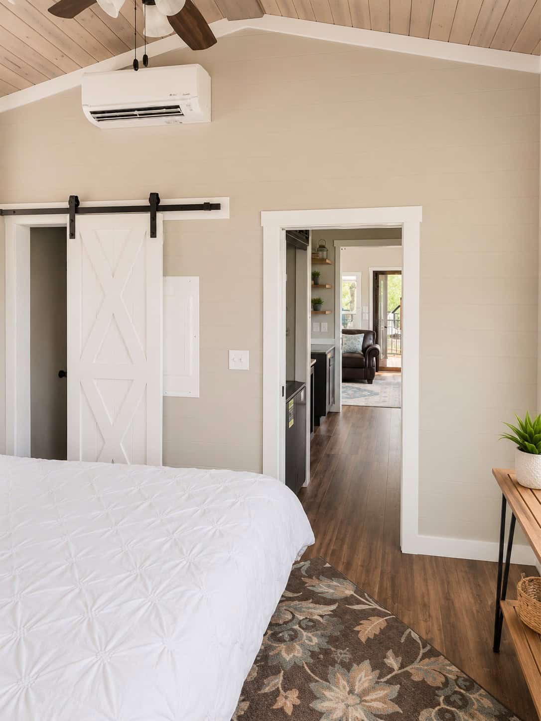 Bedroom with a white barn door, a bed in the foreground, and a hall opening toward the kitchen