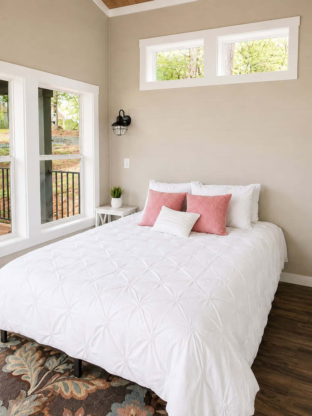 Bed against a beige wall under a triple clerestory window, with a side window to a deck