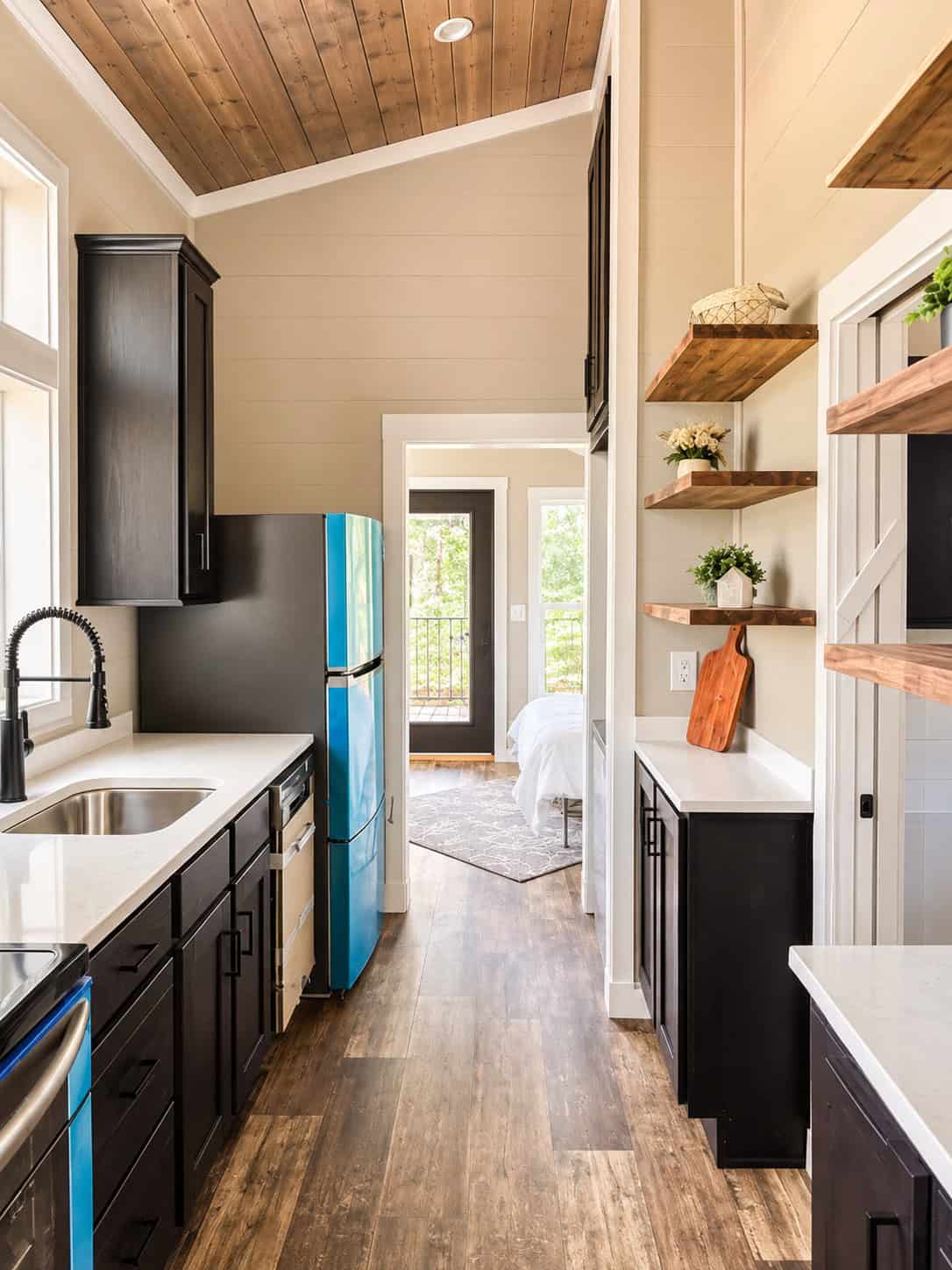 Narrow galley with dark cabinets, white counters, a stainless sink, and a bright blue refrigerator