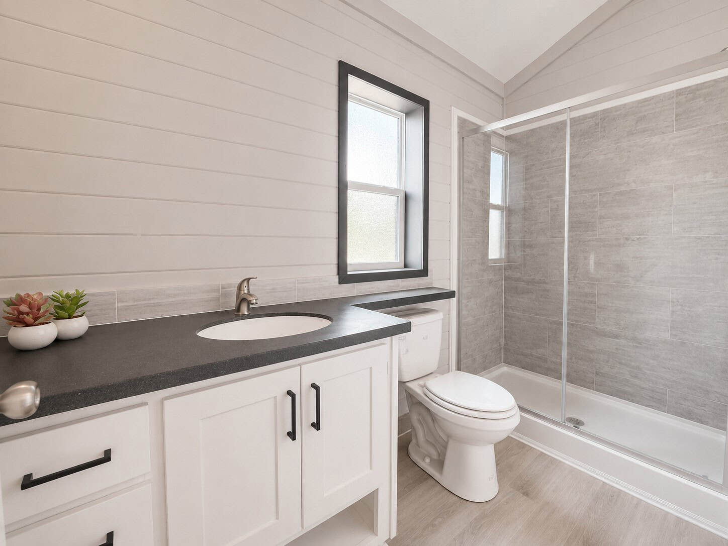 Bathroom with a white vanity, black counter, toilet, and a glass shower