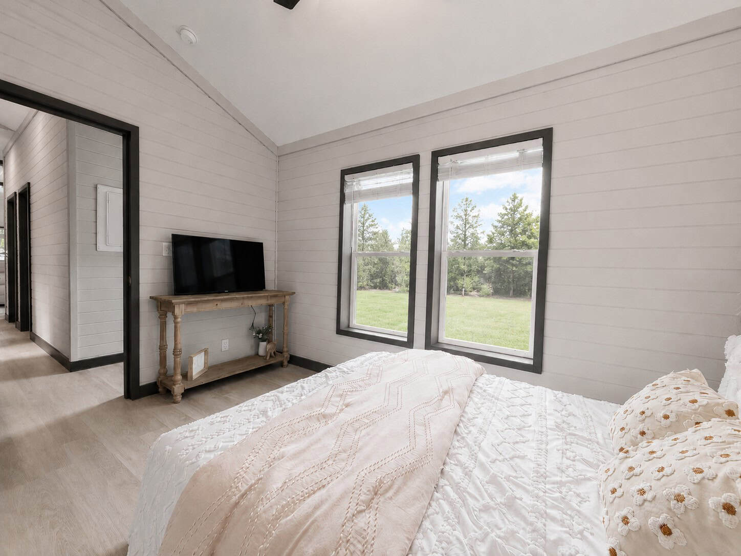 Bedroom seen from the bed toward two windows and a console with a TV
