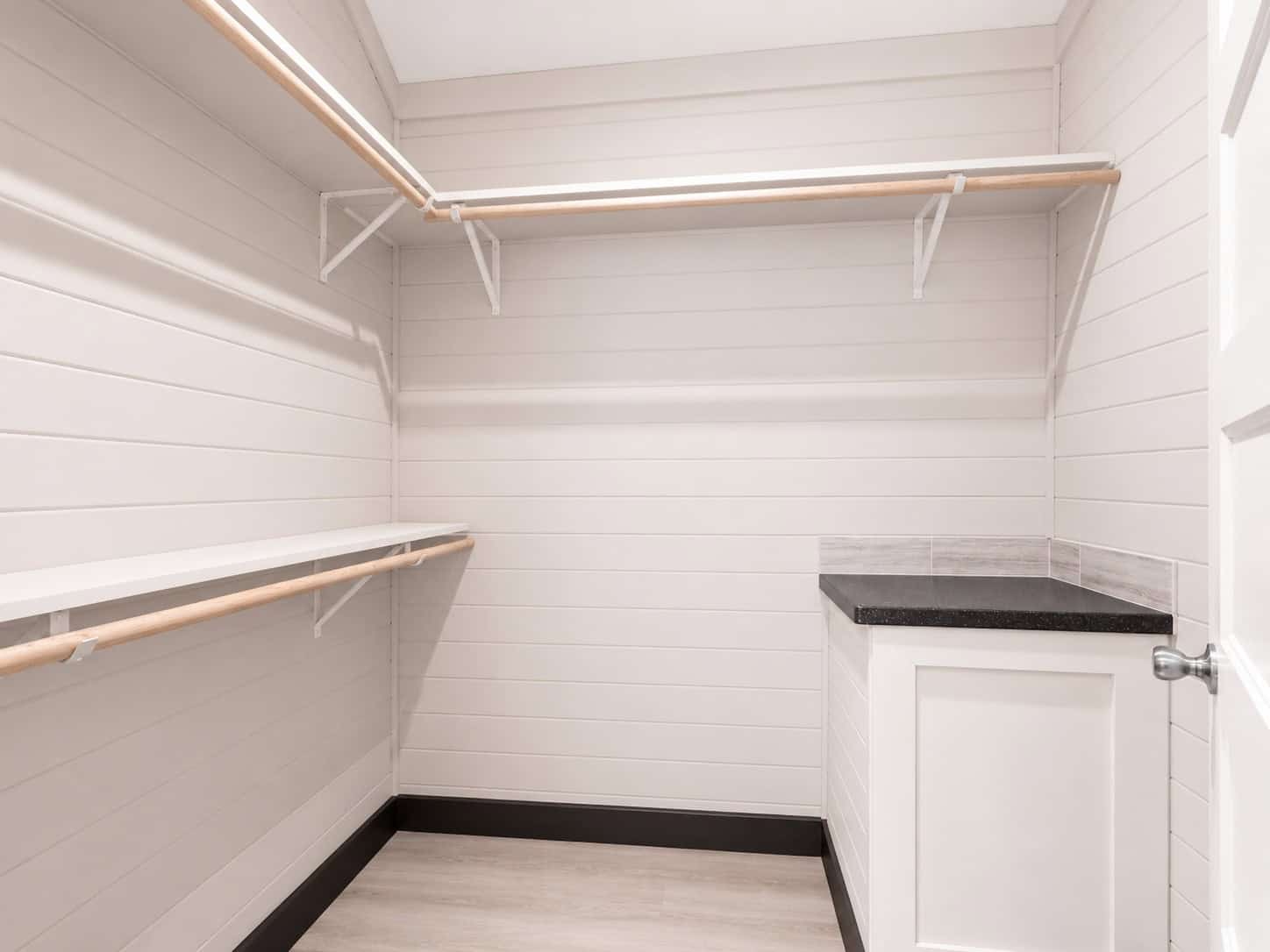Closet with wood hanging rods and a white cabinet with a black counter