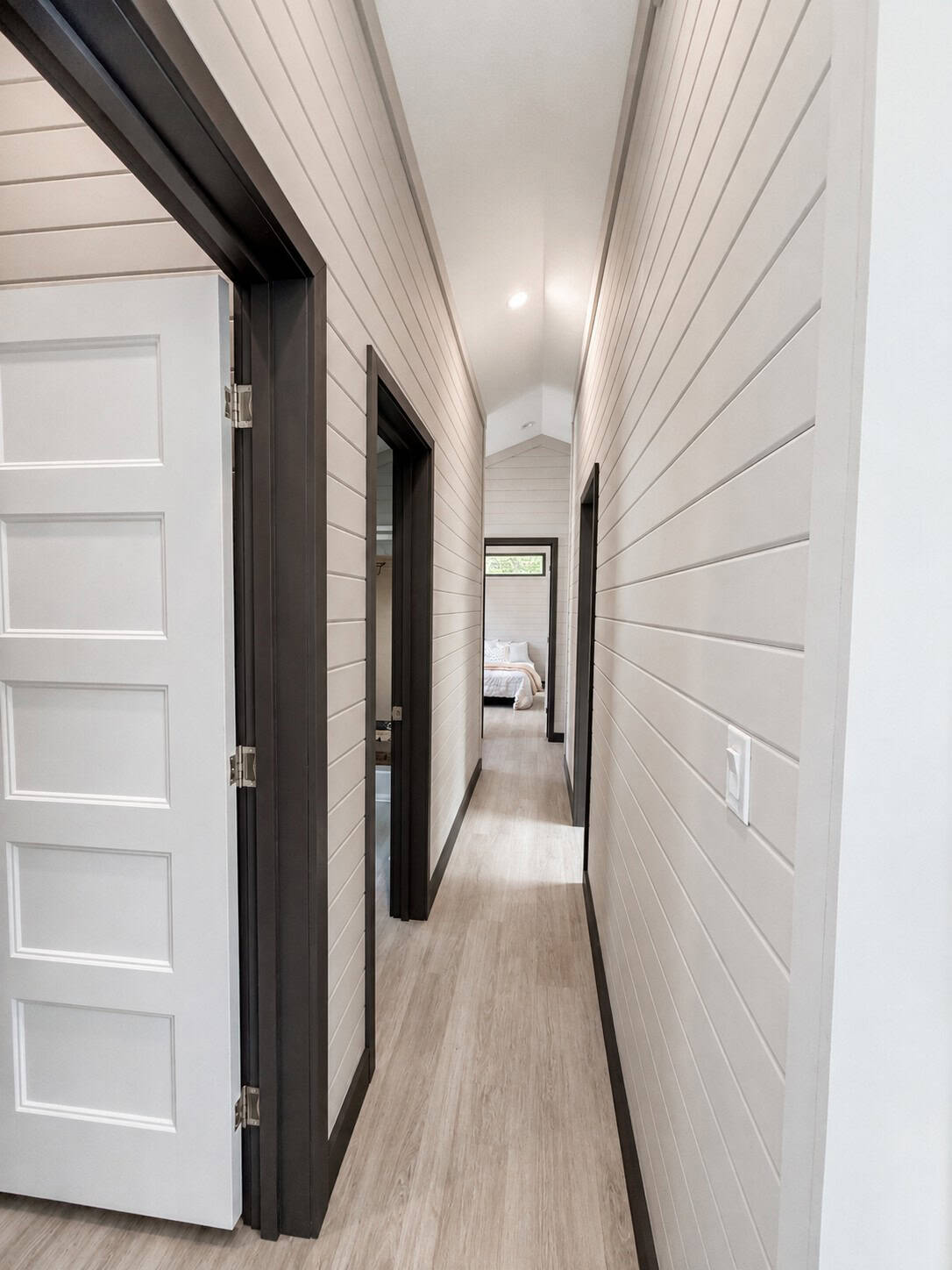 Hall with light shiplap walls, dark door trim, and a bedroom visible at the far end