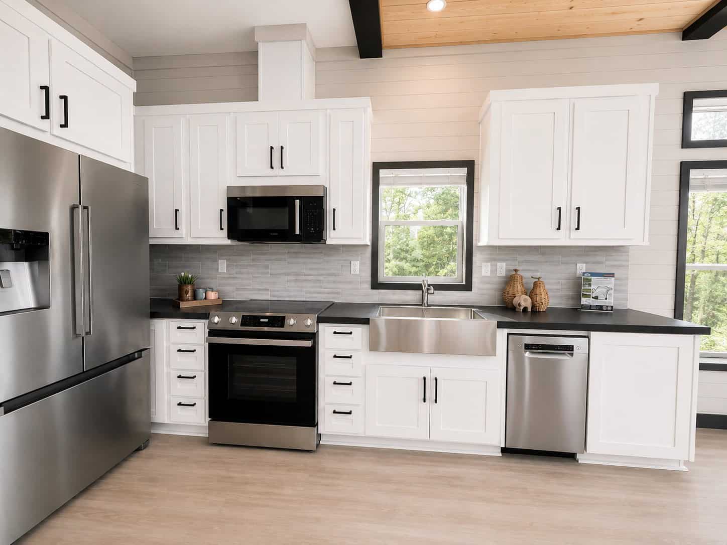Kitchen with white shaker cabinets, black counters, a farmhouse sink, and stainless refrigerator, range, and dishwasher