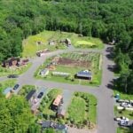 Aerial overview of Tiny Timbers Agrihood in St. Croix Falls, Wisconsin: tiny homes around a loop road with a central fenced garden, greenhouse, and solar-roofed pavilion