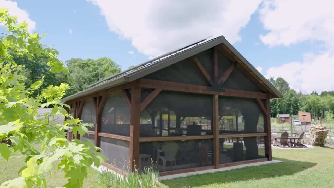 Timber-frame screened pavilion with solar panels on the metal gable roof and Adirondack chairs on the lawn at Tiny Timbers Agrihood