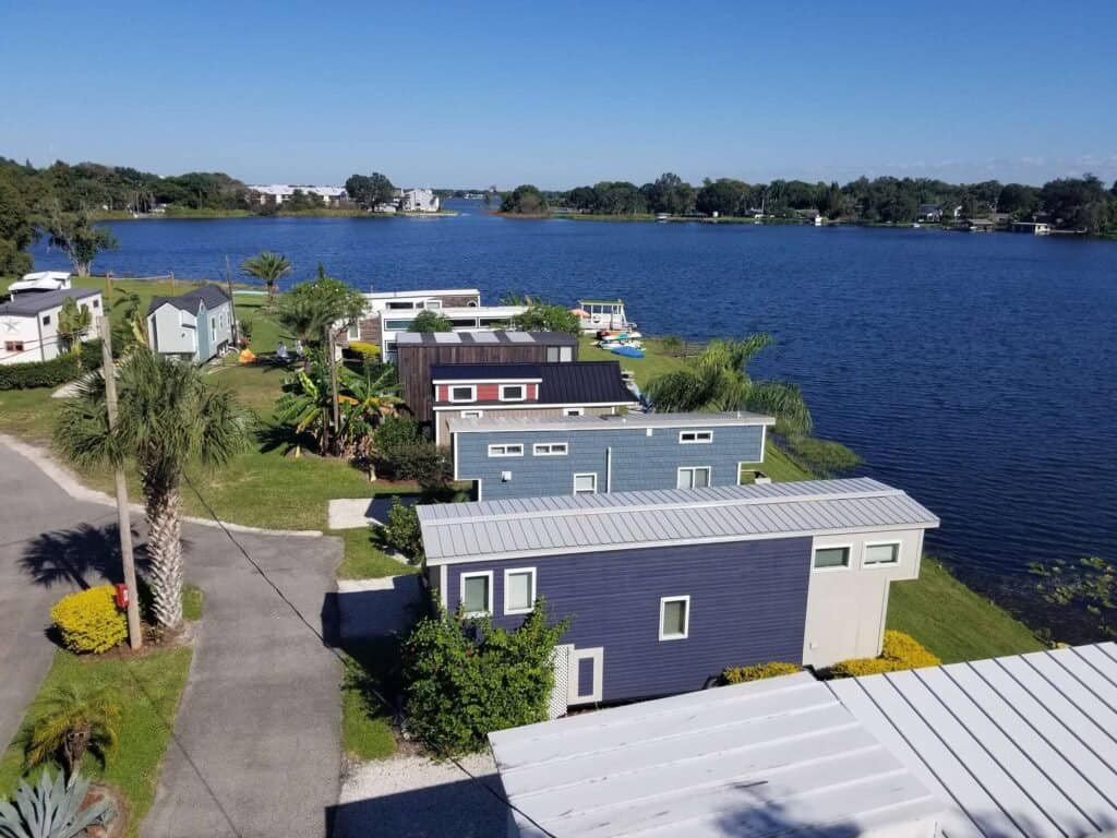 Aerial view of tiny houses in a row along Lake Fairview, a paved drive, palms, and docks at the shore at Tiny Town Orlando
