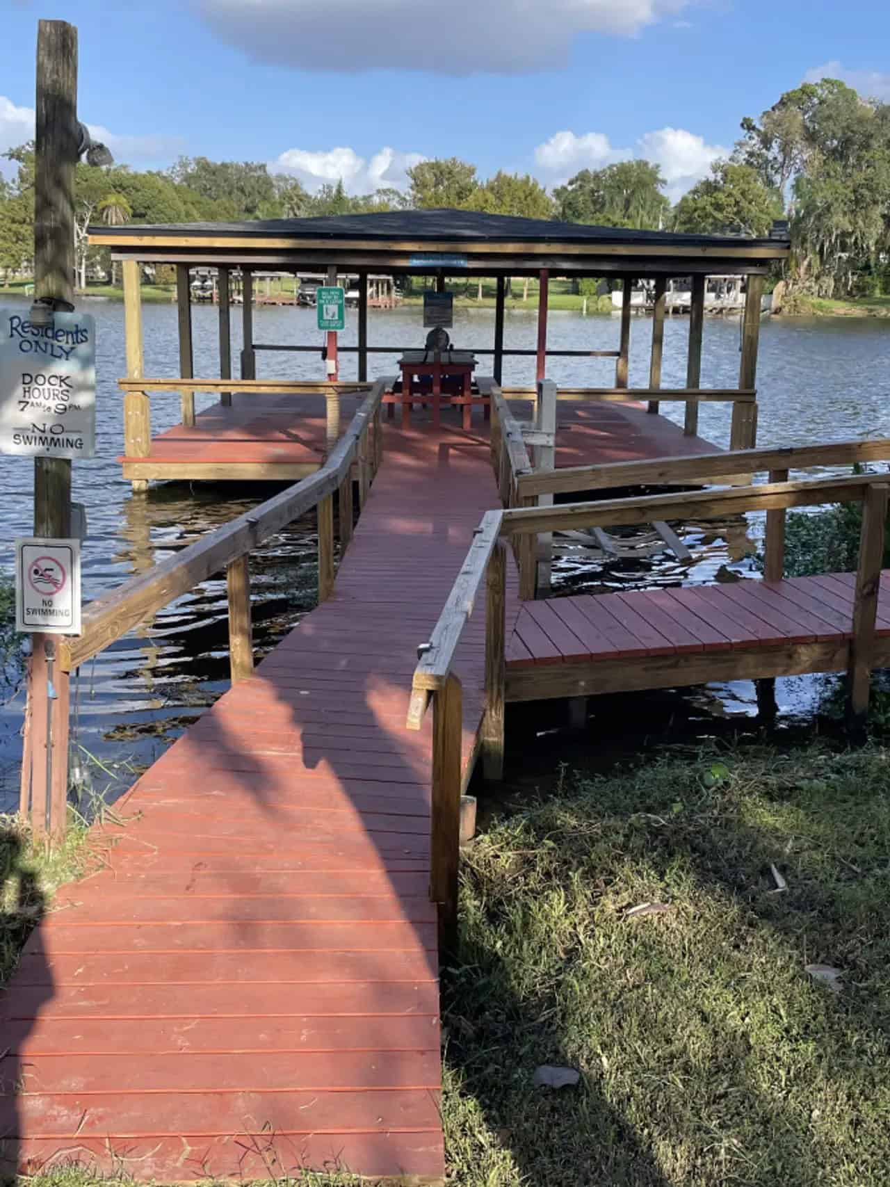 Red wooden walkway to a covered dock on Lake Fairview with a residents-only hours sign at Tiny Town Orlando