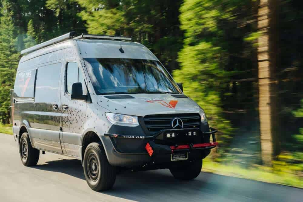 Silver Titan Vans Mercedes Sprinter camper conversion driving a forest road, roof rack and front guard visible