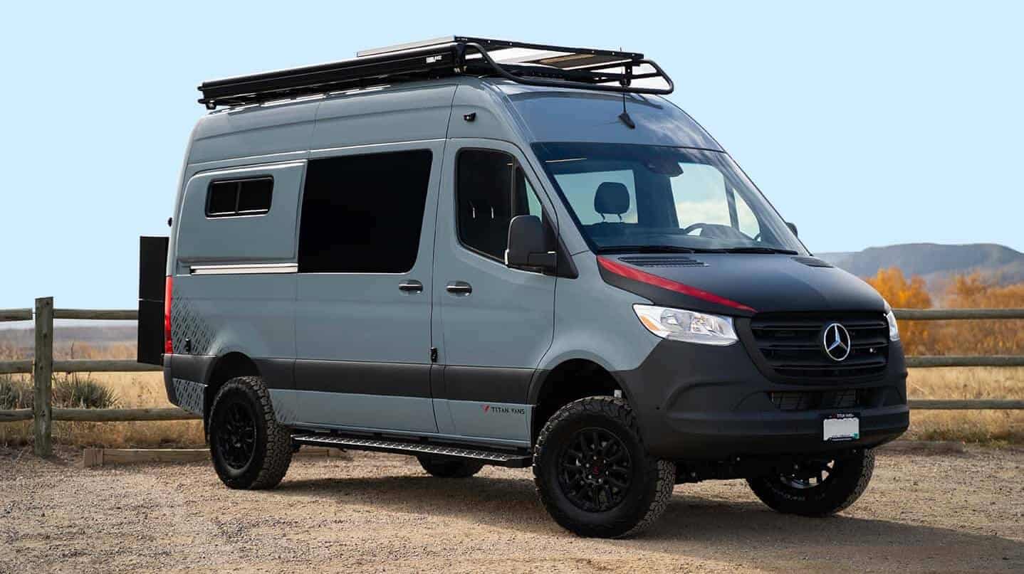 Light blue-grey Titan Vans Mercedes Sprinter camper conversion parked on a dirt path with roof rack and awning