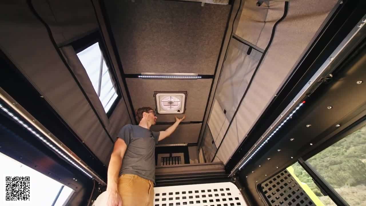 Looking up at the Badlands camper ceiling with optional carpet-wrapped insulation and a square Maxxair fan, host's hand near the vent