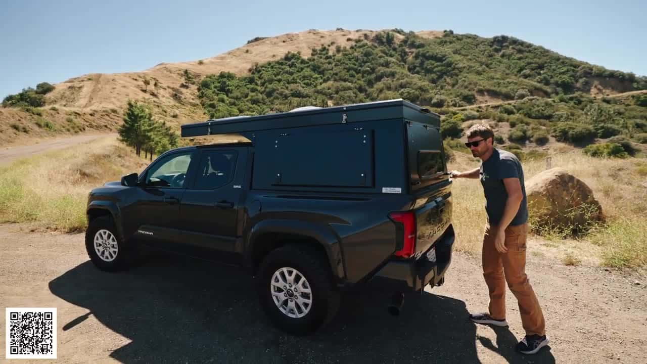 High-angle view of a Tacoma with the Badlands camper closed low for travel, host at the rear corner in dry hills