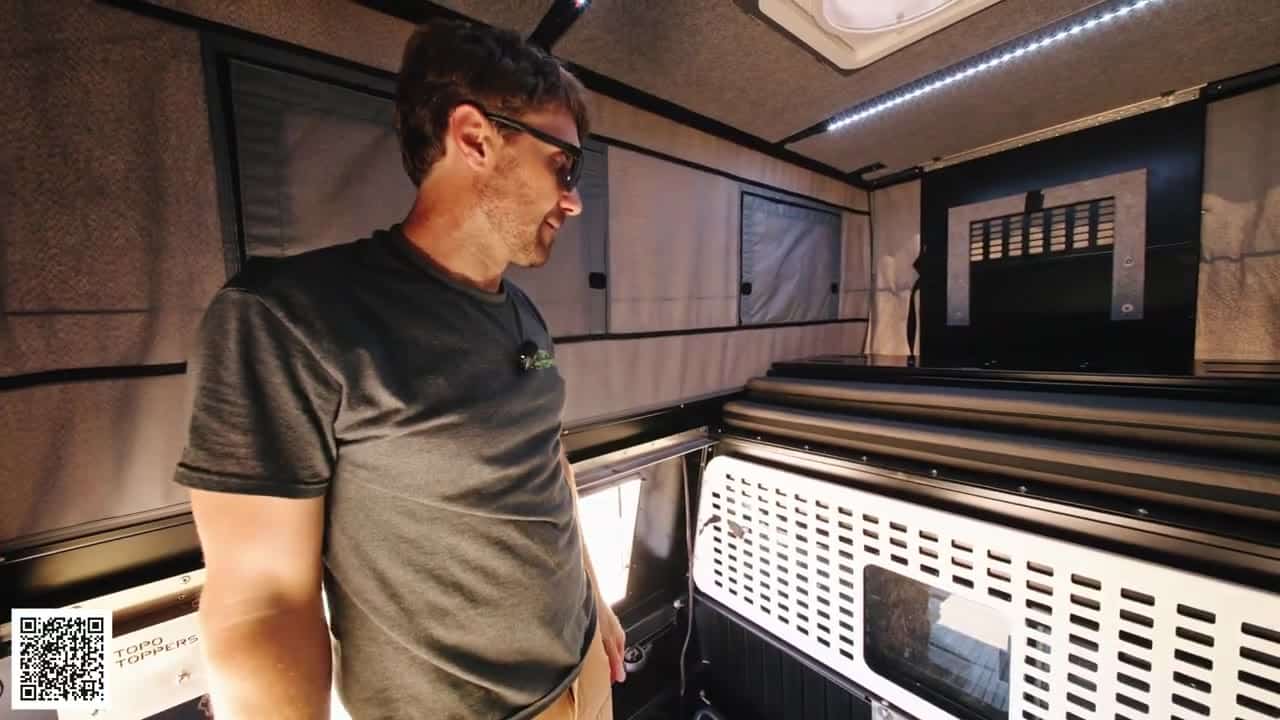 Interior of the Badlands camper looking toward the cab, mattress sections stacked forward, cab-side MOLLE panel, insulated ceiling and LED strip
