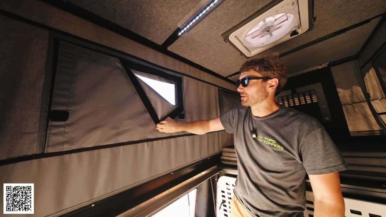 Host peeling back a Velcro tent-window cover on the gray fabric wall of the Badlands pop-up camper