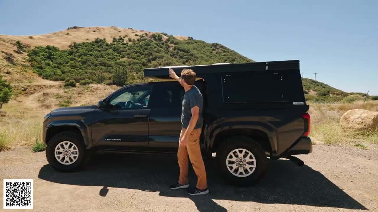 Side view of a Toyota Tacoma with the Topo Toppers Badlands aluminum canopy closed and low-profile, host standing by the driver door in dry hills