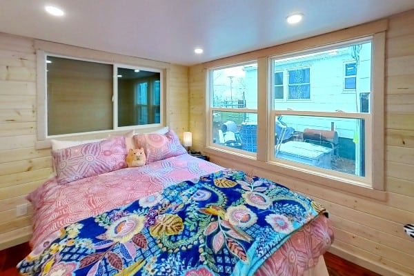 Downstairs Elm bedroom: light pine plank walls, white ceiling, colorful patterned bedding, sliding window one side and sash windows the other