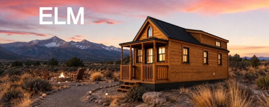 Honey-cedar Tumbleweed Elm on a trailer at dusk: gothic-arch window over a covered porch with turned posts, stone fire pit and Adirondack chairs, snow-capped mountains, ELM wordmark