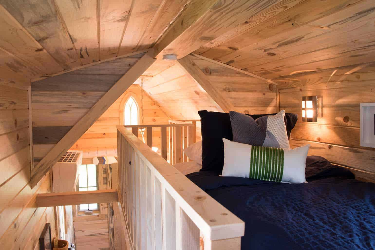 Elm sleeping loft: light wood planks, navy bedding, slat railing, gothic-arch window in the gable peak