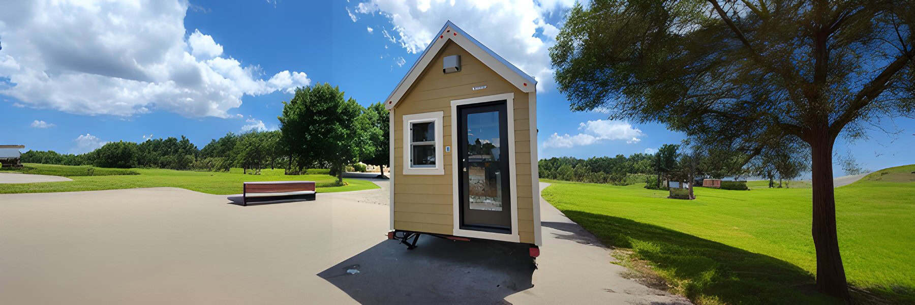 Tan Tumbleweed Farallon tiny house on a dual-axle trailer: steep silver gable, white trim, black-framed glass door, parked on pavement under a blue sky