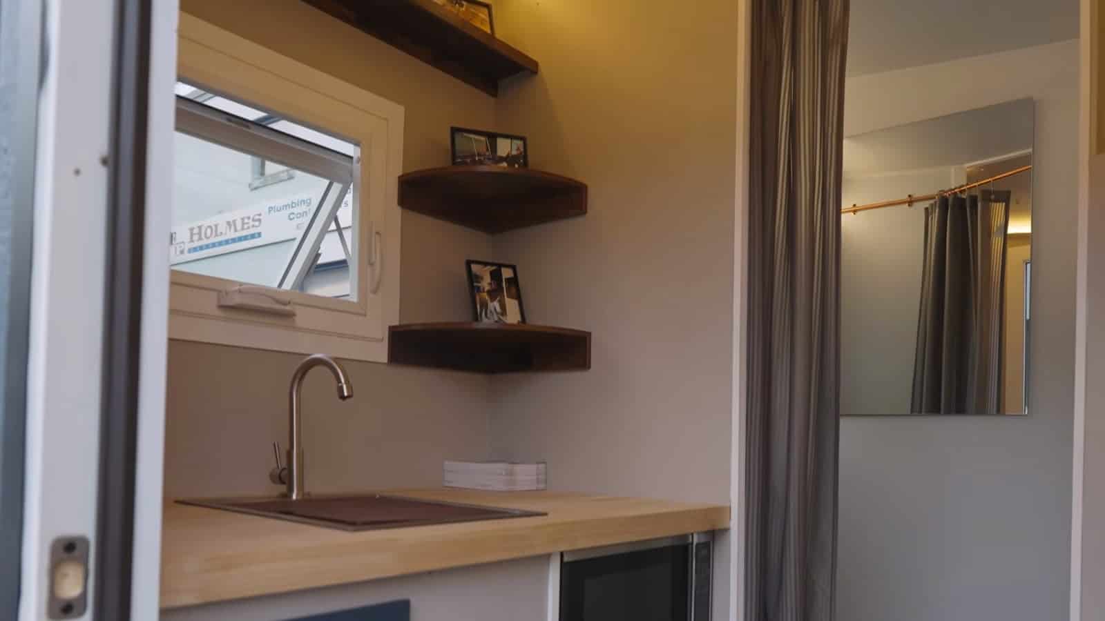 Compact kitchen inside the Uplift Micro Home with sink, wood counter and floating shelves
