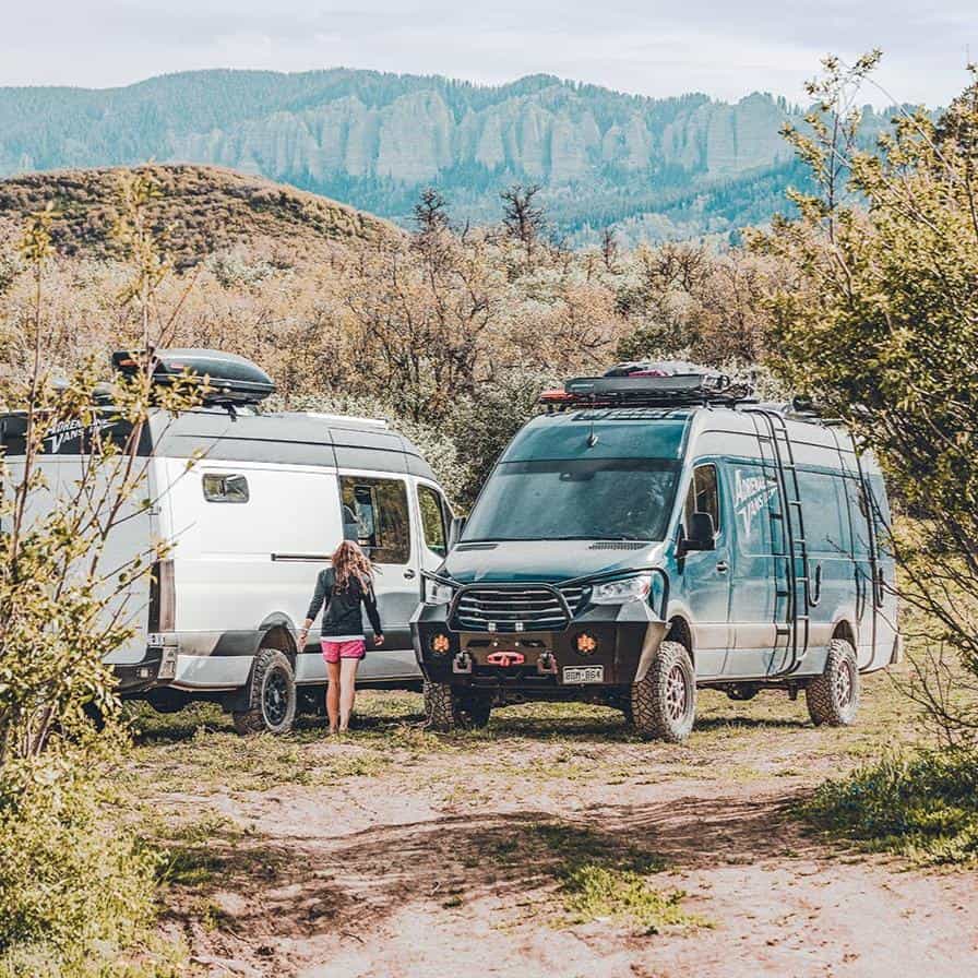 Two Adrenaline Vans Sprinters parked in grass with Colorado mountains behind them